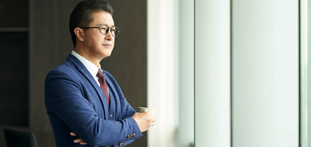 Asian senior manager in a suit looking out a window.
