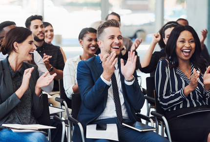 An audience in business attire clapping and cheering during a conference.