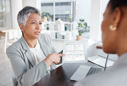 A business woman pointing towards a tablet while talking to a client.