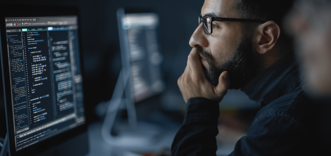 A male student coding on a computer with his head resting on one hand.